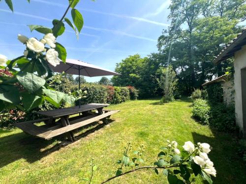 a picnic table with an umbrella in a garden at L'Échappée Verte - Maison familiale avec Jardin & Parking - 20 min du PuyduFou in Mauléon