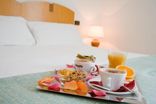 een dienblad met ontbijtproducten en drankjes op een bed bij Grand Hotel Mediterraneo in Santa Cesarea Terme