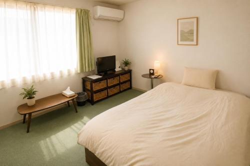 a bedroom with a white bed and a television at ゲストハウスガーデンズmihama in Wada