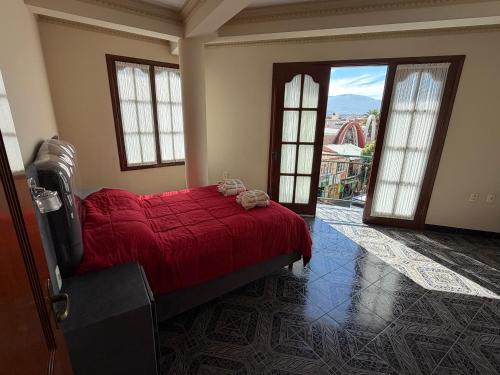 a bedroom with a bed with a red comforter and large windows at Altos de Belgrano Suites in Tarija
