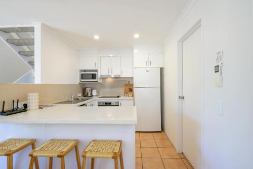 a kitchen with white cabinets and a white refrigerator at Riverside Retreat, Noosaville in Noosaville