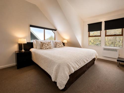 a bedroom with a large bed and two windows at Cape Cod Chalet, alpine-getaways in Dinner Plain