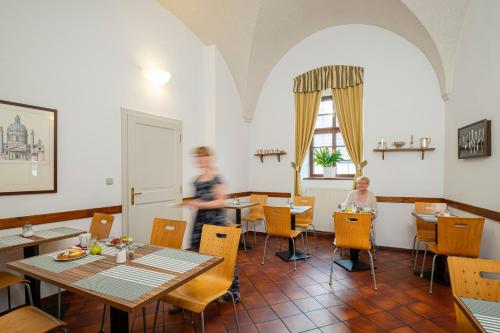 a man is standing in a restaurant with tables and chairs at Hotel Adalbert in Prague