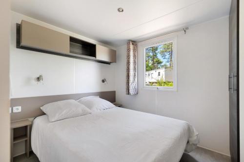 a bedroom with a white bed and a window at Bungalow Cap Ferret Les Lodges 3 in Lège-Cap-Ferret