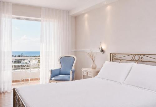 a bedroom with a bed and a blue chair and a window at Lagos Mare Hotel in Agios Prokopios