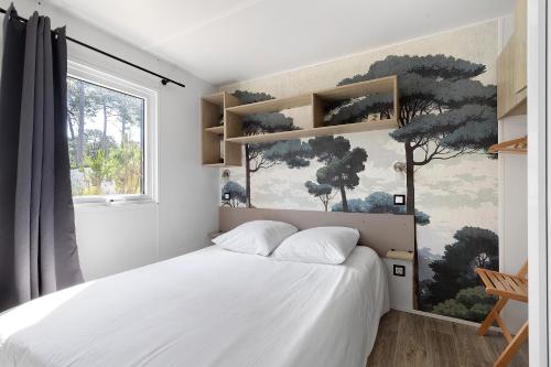 a bedroom with a white bed and a window at Bungalow Cap Ferret Les Lodges 2 in Lège-Cap-Ferret