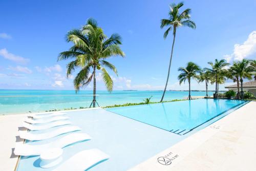 a swimming pool with palm trees and the ocean at 2 Bed Ocean View Condo at ONE Cable Beach in Nassau