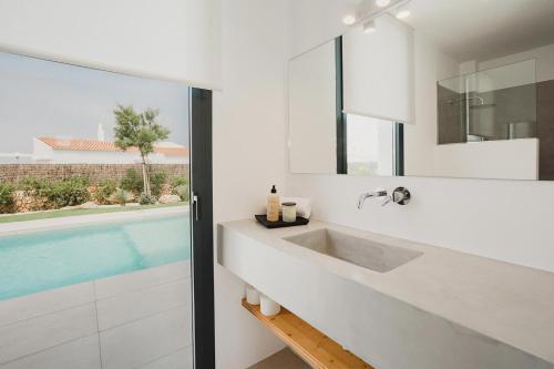a white bathroom with a sink and a swimming pool at Canalola in Cala en Bosc