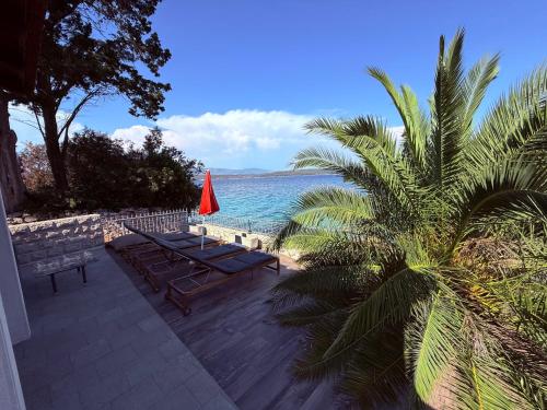 a beach with benches and a red umbrella at Villa Mala Dora in Stari Grad
