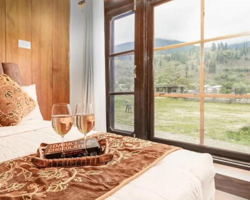 two glasses of wine on a bed with a view of a field at kanwal cottages safa resort in Dandpur