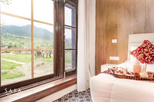 a bedroom with a bed and a large window at kanwal cottages safa resort in Dandpur