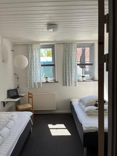 a bedroom with two beds and a desk and two windows at Ibsens Gaard in Ebeltoft
