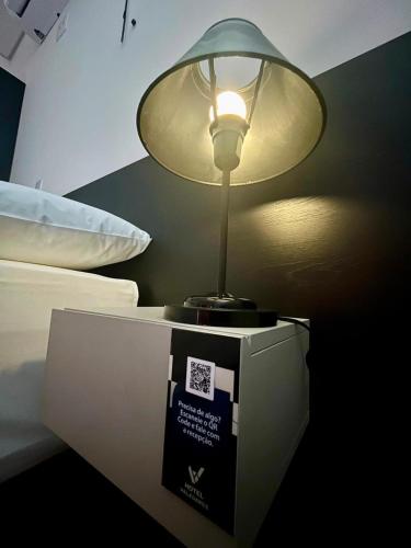 a lamp sitting on top of a table next to a bed at Hotel Valadares in Alfenas