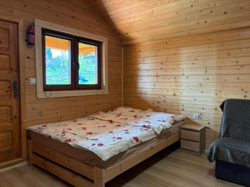a bed in a wooden room with a window at POD FALAMI - domki letniskowe in Polańczyk