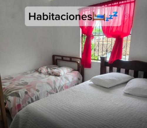 a bedroom with two beds and a window with red curtains at Casa de Descanso la Cascada in Sopetrán