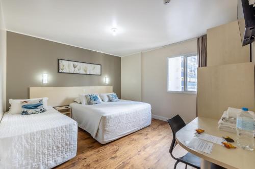 a hotel room with two beds and a table at Hotel Bella Camboriú in Balneário Camboriú