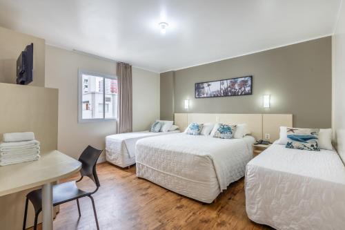 a hotel room with two beds and a desk at Hotel Bella Camboriú in Balneário Camboriú