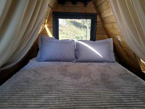 a bed with pillows in a room with a window at Vale do Sossego- Cabana na Serra in Alfredo Wagner