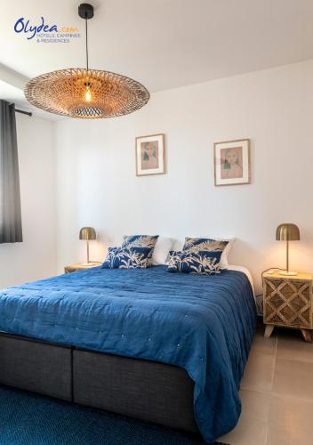 a bedroom with a blue bed and a chandelier at Olydea Beausoleil in Beausoleil