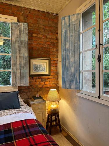 a bedroom with a bed and a lamp and windows at Piccola Cucina: Casa centenária Vale dos Vinhedos in Garibaldi