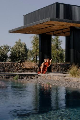 a woman sitting on a bench next to a body of water at Scorzamara Country Lodges - Retreats with Private Pool or Jacuzzi in Carlentini