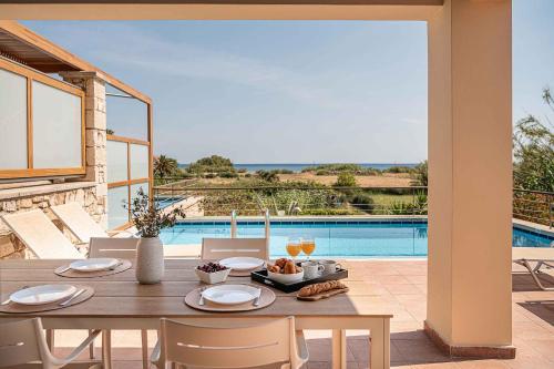 a dining table and chairs with a view of a pool at Corali Villas - Seaview, Private Pools, 450 to Beach in Kolymvari