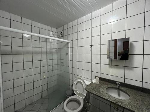 a white tiled bathroom with a toilet and a sink at Pousada Requinte in Vila Velha