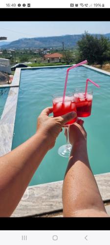 a person holding a drink in front of a pool at Kalanar villa in Elbasan