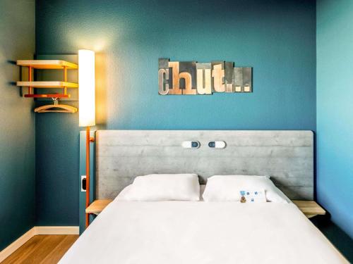 a bedroom with a white bed with a blue wall at ibis budget Pertuis Portes du Luberon in Pertuis