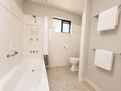 a white bathroom with a tub and a toilet at Alex Headland Unit Views to the Ocean in Alexandra Headland