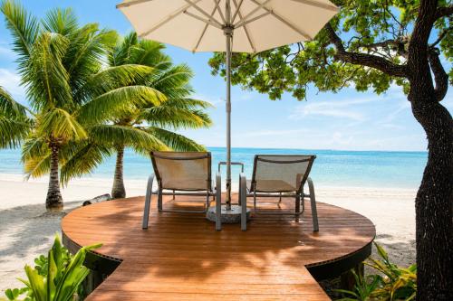 two chairs and a table with an umbrella on the beach at Aitutaki Escape Resort & Spa in Arutanga
