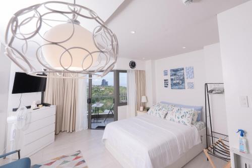 a white bedroom with a bed and a chandelier at Deluxe Studio-Condo at Tambuli Seaside Living in Maribago
