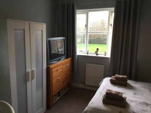a bedroom with a bed and a tv and a window at Constantine Court Homestay in Shepton Mallet