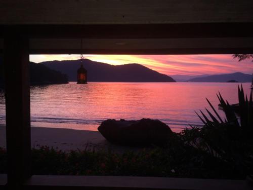 a sunset over a body of water with a lighthouse at Bonito Paraiso Ilha Grande in Abraão