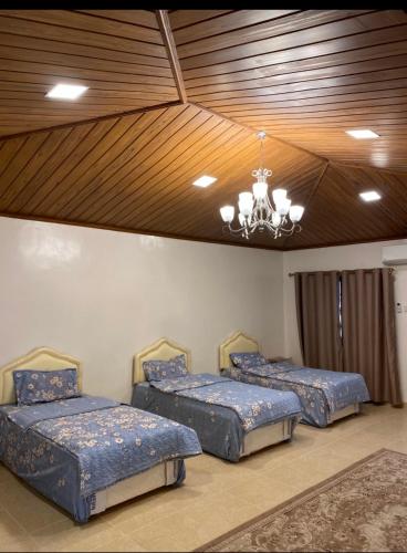 three beds in a room with a chandelier at استراحة الروابي in Salalah