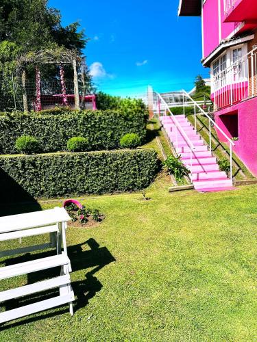 a pink building with a white bench in the grass at Pink Village Boutique in Campos do Jordão