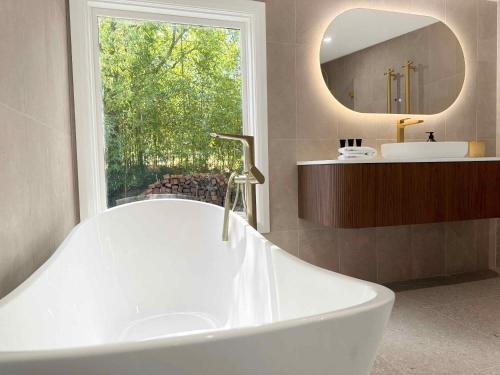 a large white tub in a bathroom with a window at Highwoods Cottage in Pokolbin