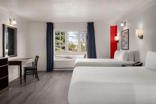 a hotel room with two beds and a desk and a window at Ramada by Wyndham Laval in Laval