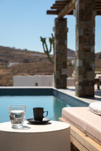 a glass of water and a cup on a table next to a pool at Villa Lefko in Ano Syros