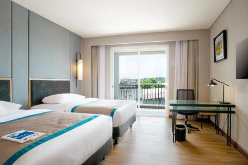 a hotel room with two beds and a desk and a window at Blue Sky Hotel Balikpapan in Balikpapan