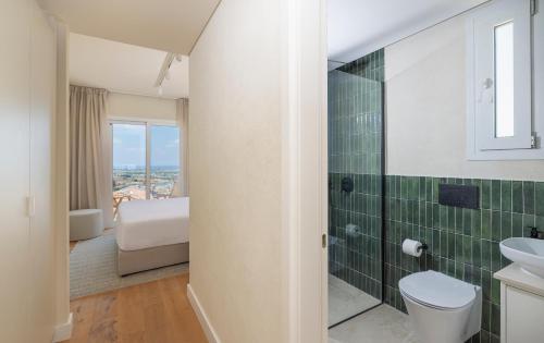 a bathroom with a toilet and a green tiled wall at WellClub Resort - Suites & Wellness in Paphos
