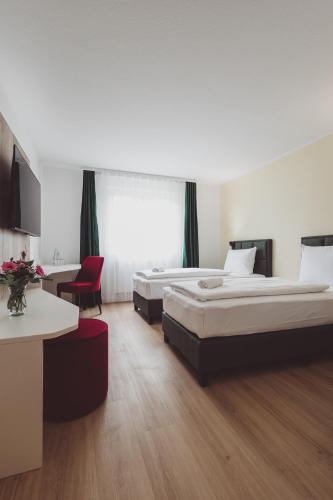a hotel room with two beds and a red chair at Hotel City Green Hoppegarten in Hoppegarten