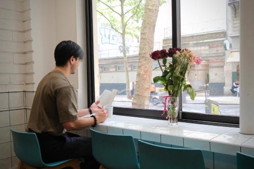 a man sitting in a chair reading a paper next to a window at Hipotel Paris Gambetta République in Paris