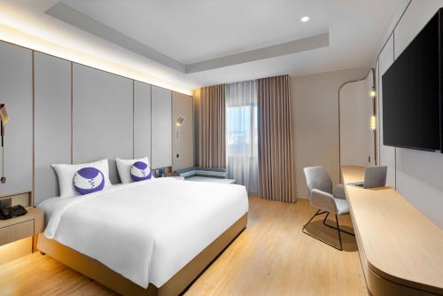 a hotel room with a large white bed and a desk at Fox Hotel Nagoya Batam in Nagoya