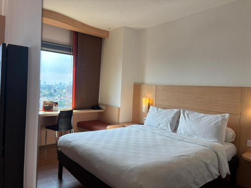 a hotel room with a bed and a desk and a window at Swiss-Belinn Cawang in Jakarta