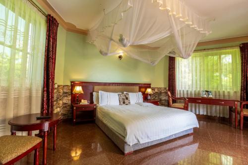 a bedroom with a bed and a table and windows at Asamar Country Resort in Mbarara