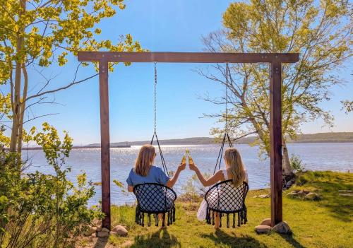 two women sitting in chairs on a swing by the water at Condo 1 - Waterfront with SPA, Fireplace & Barbecue in Sainte-Anne-de-Beaupré