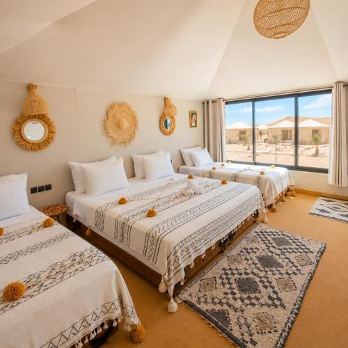 a bedroom with three beds and a large window at Sinbad Merzouga Camp in Merzouga