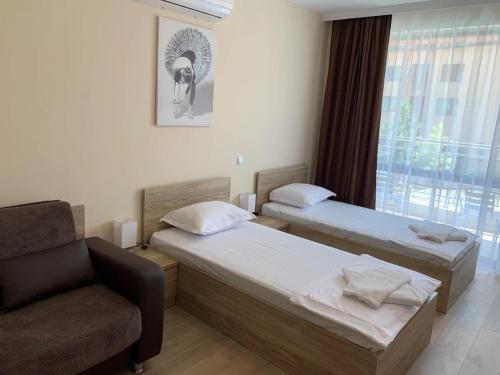 a room with two beds and a chair and a window at Cattleya in Nesebar