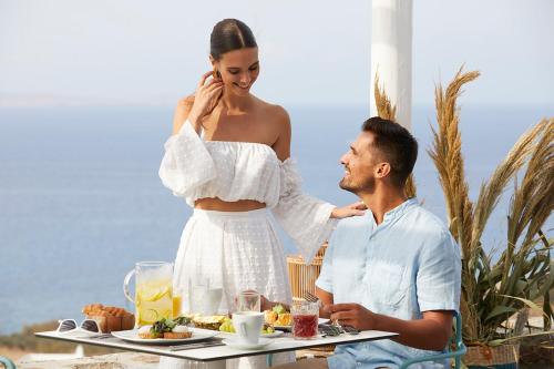 a man and a woman sitting at a table with food at Epic Blue Mykonos in Houlakia